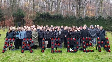Auf einer Wiese steht eine große Gruppe junger Menschen, die isch hinter dem Schriftzug "Frieden" versammelt hat.