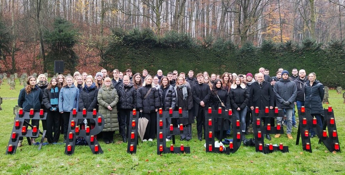 Auf einer Wiese steht eine große Gruppe junger Menschen, die isch hinter dem Schriftzug "Frieden" versammelt hat.