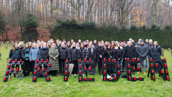Auf einer Wiese steht eine große Gruppe junger Menschen, die isch hinter dem Schriftzug "Frieden" versammelt hat.